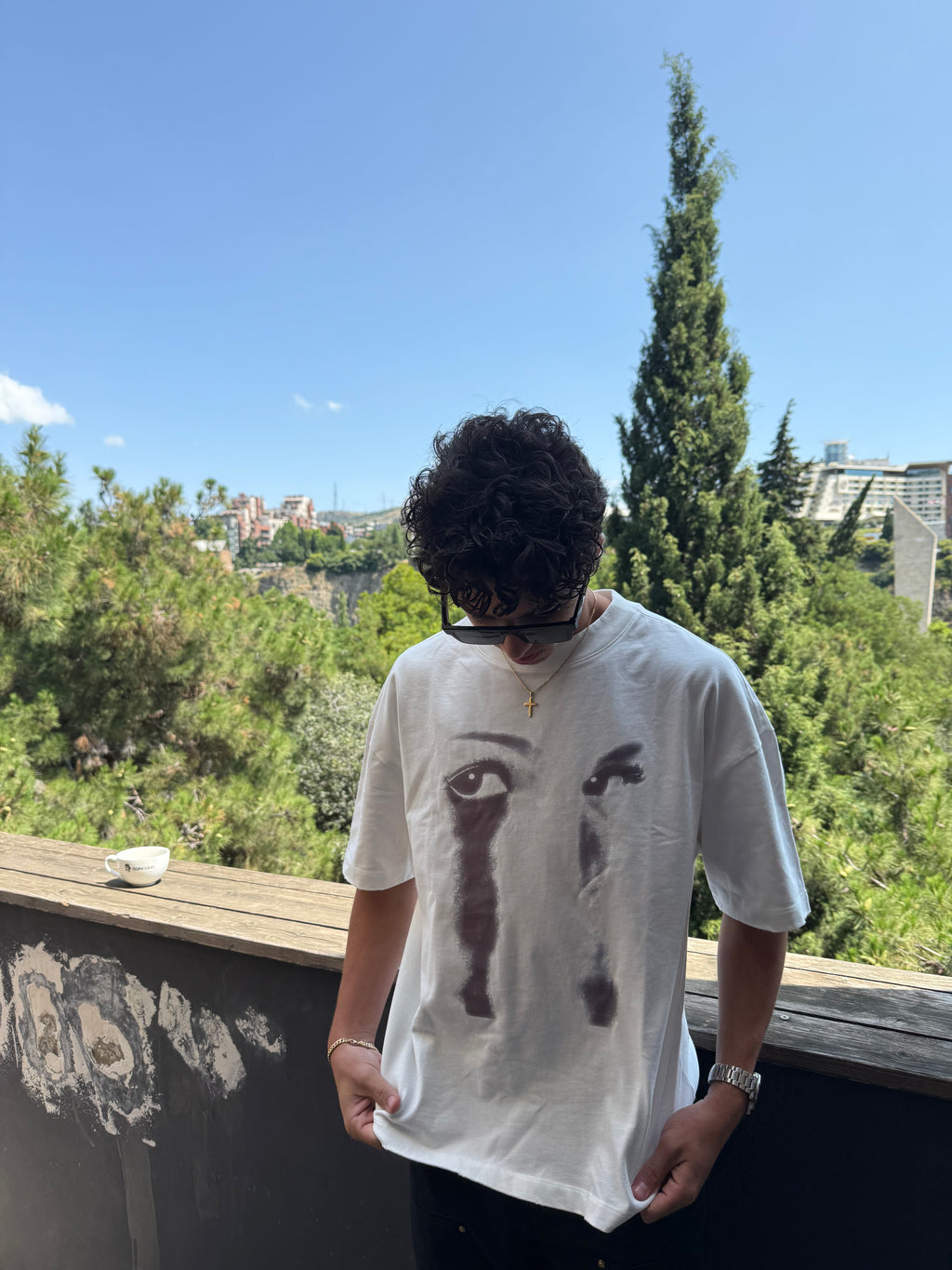 Person wearing a white t-shirt with black graphics outdoors on a sunny day.