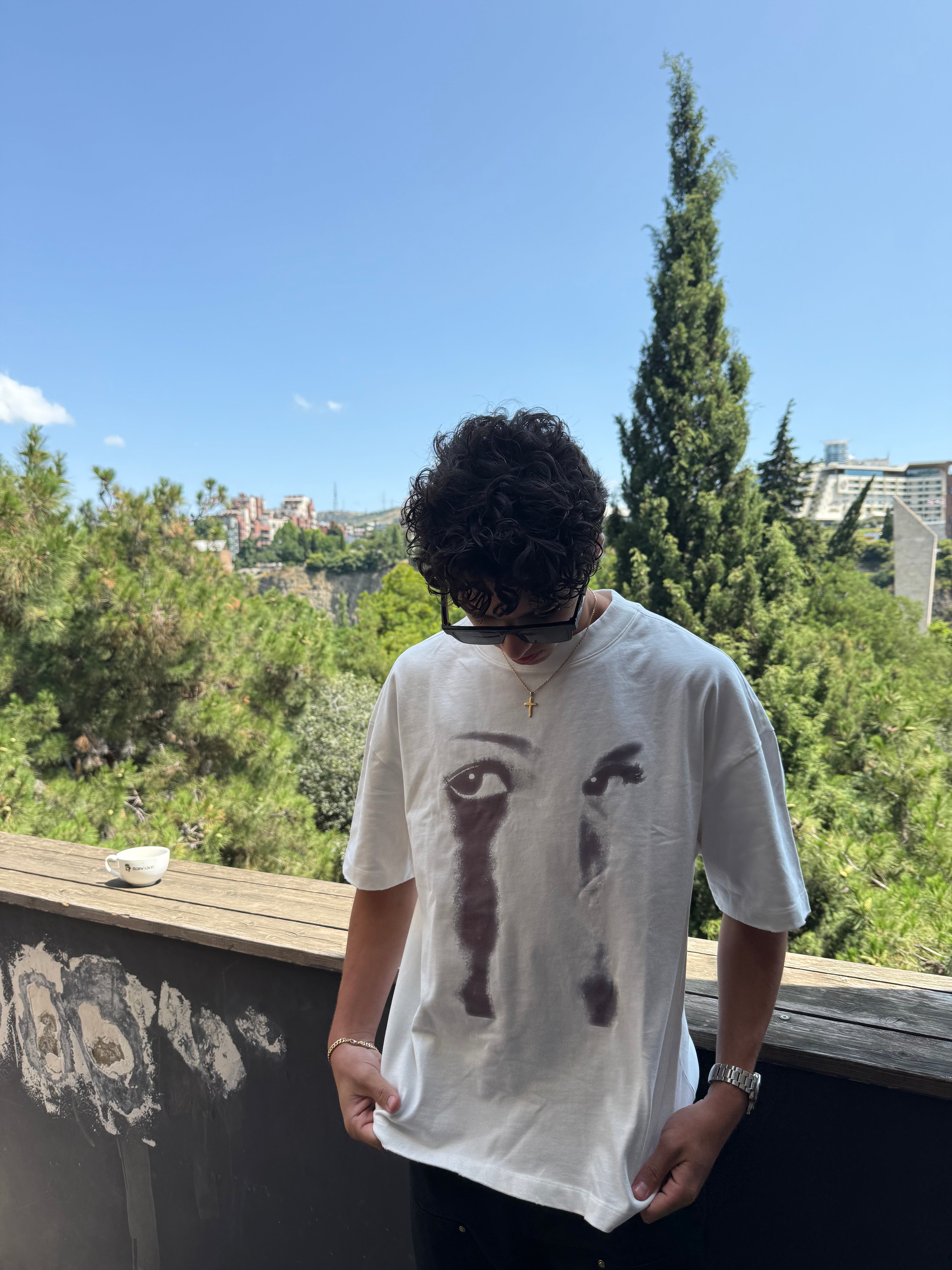 Person wearing a white t-shirt with black graphics outdoors on a sunny day.