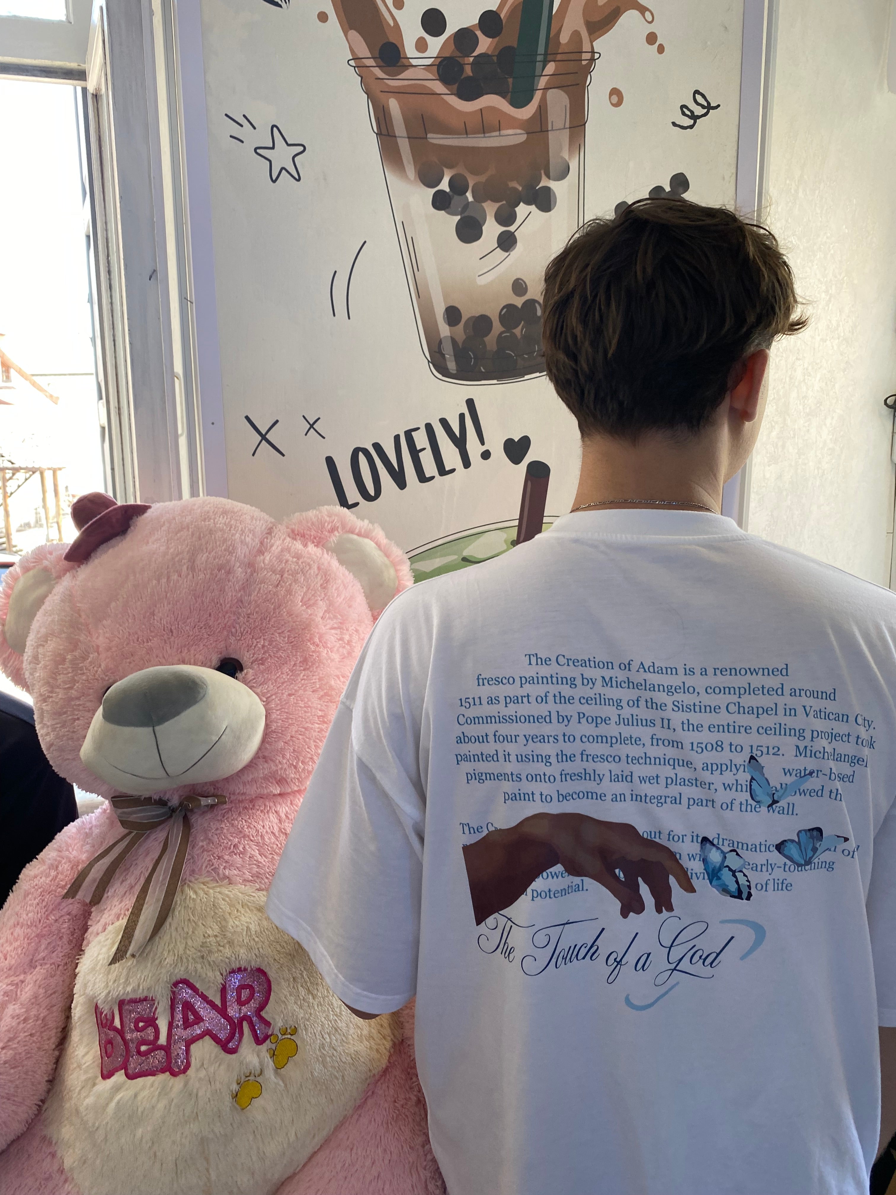 Person wearing a white t-shirt with text and graphics, holding a pink teddy bear.