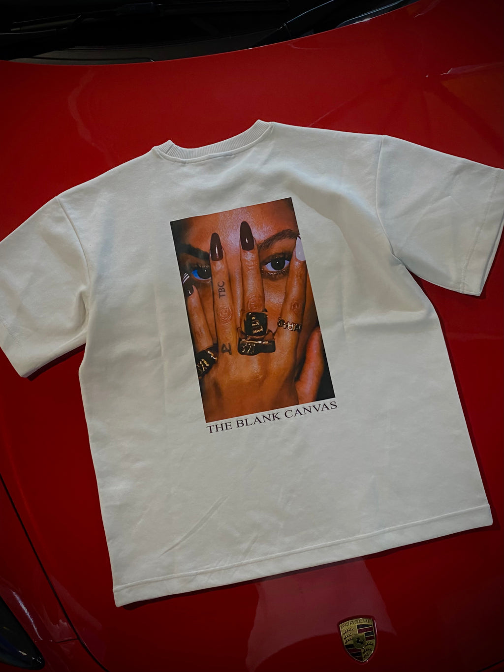 White t-shirt with a graphic of a hand with rings and 'The Blank Canvas' text on a red surface.