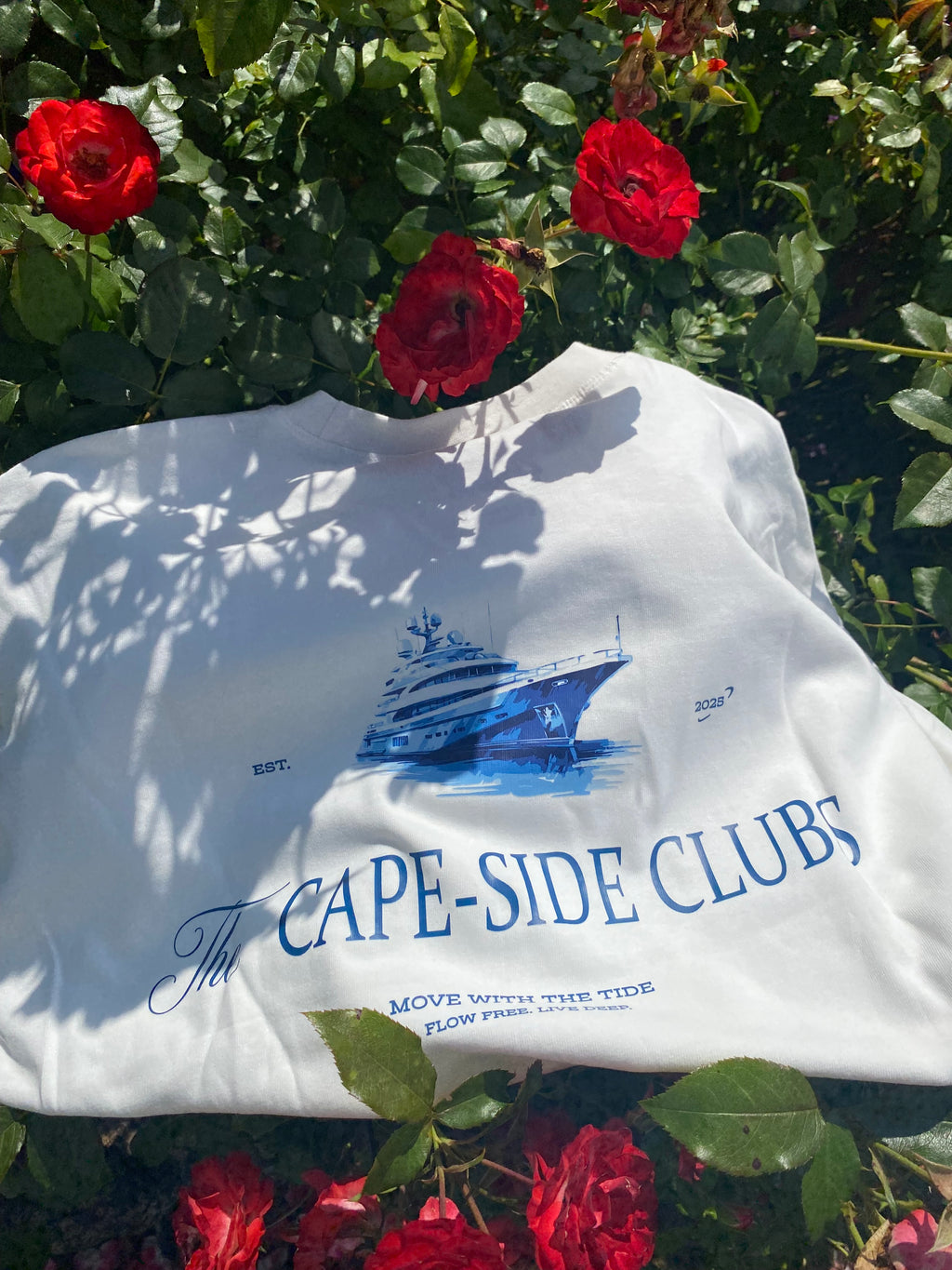 White shirt with blue text and graphics on a background of red roses and green foliage