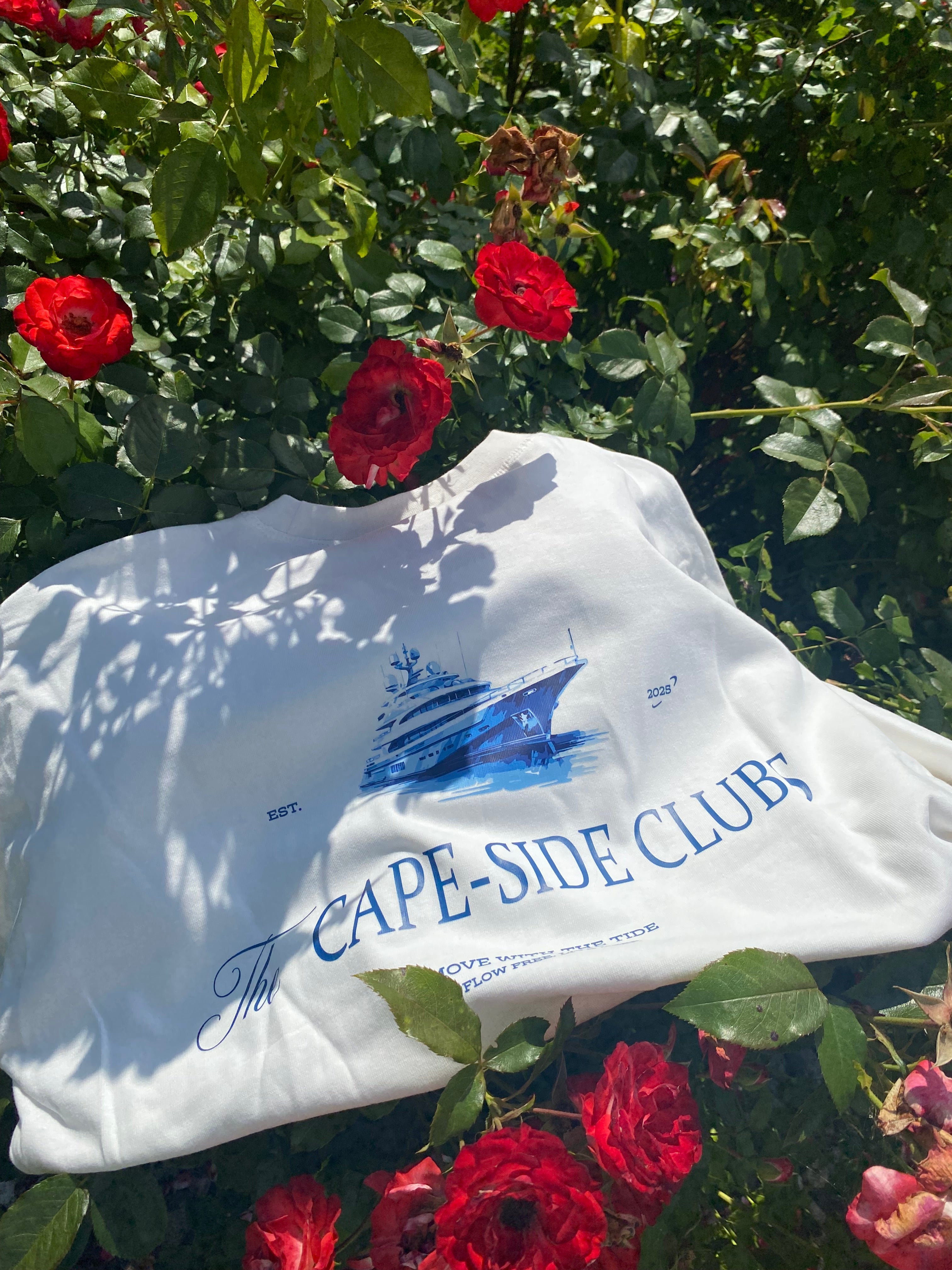 White shirt with blue text and graphics on a background of red roses and green foliage