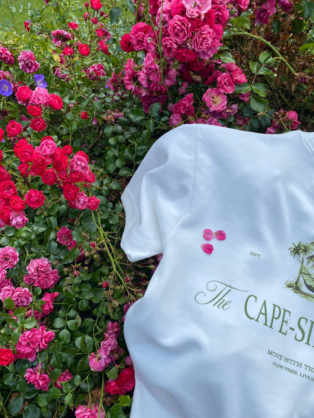 White shirt bag with 'The Cape Side Ckubs' branding on a bed of pink and red flowers.