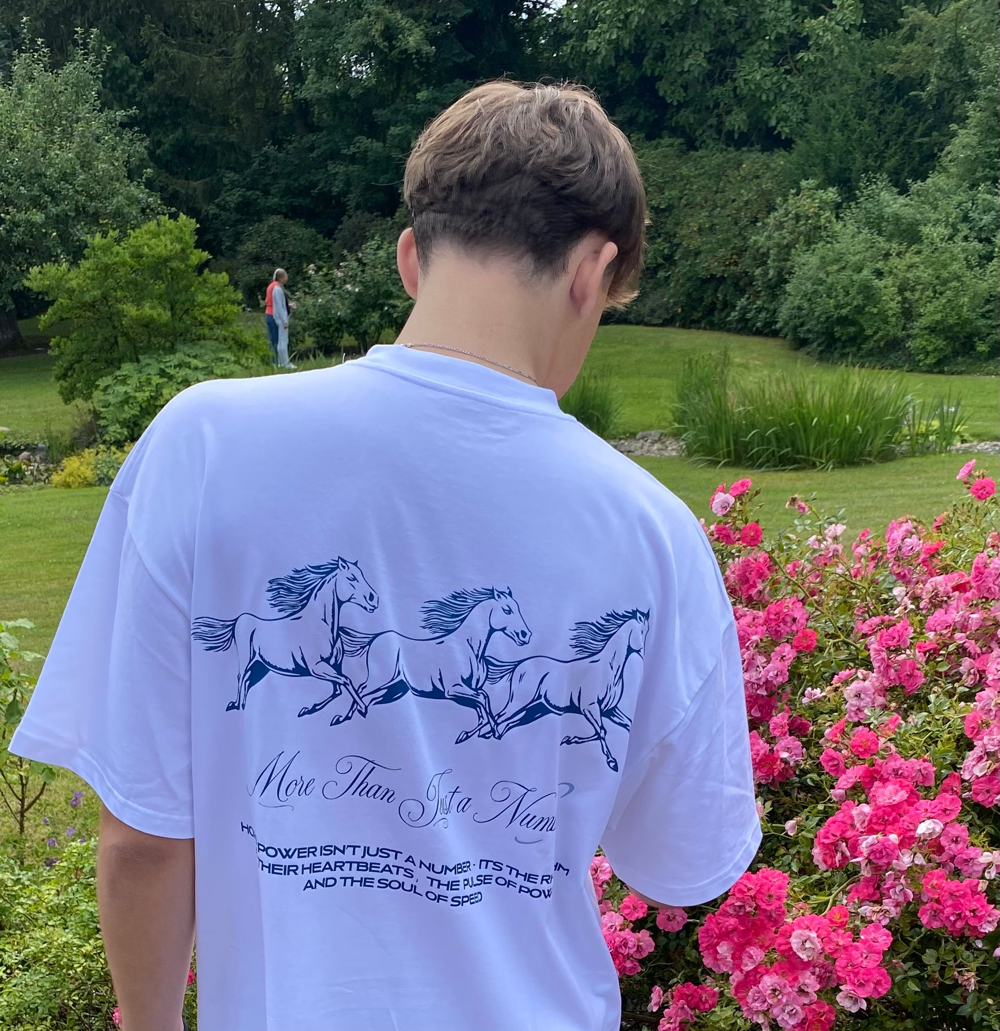 Person wearing a white t-shirt with horse design and text in a garden setting